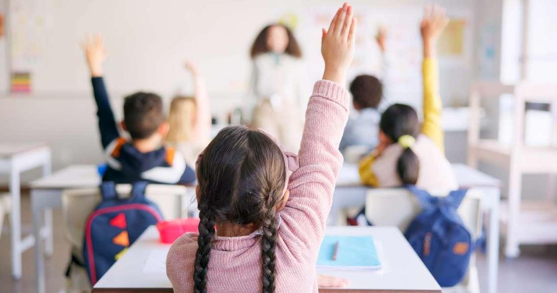 Students raising their hands in a classroom (Photo by: Jacob Wackerhausen/ iStock / Getty Images Plus)